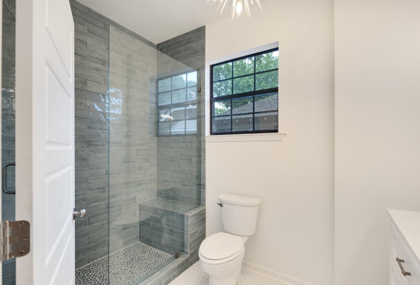 Glass-enclosed shower with gray stacked tile, a pebble-finish floor, and built-in bench