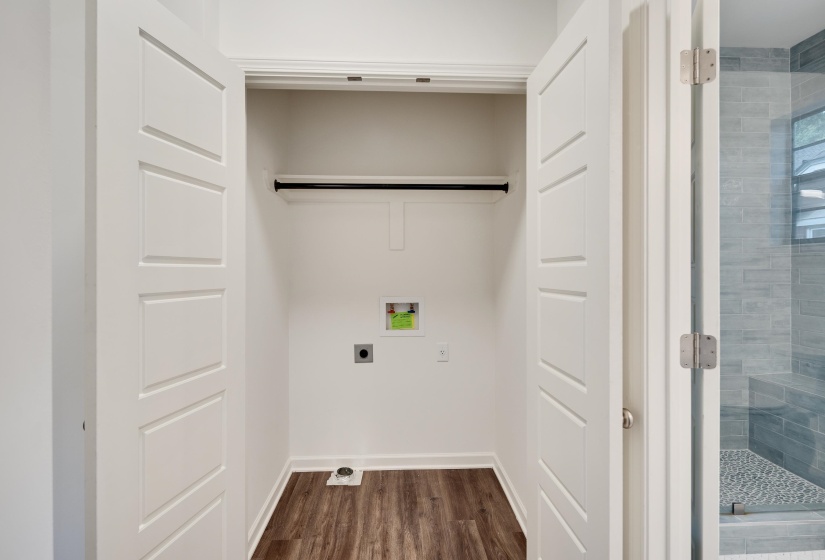 Dedicated laundry closet featuring wood-finish flooring, a hanging rod, appliance hookups, and bi-fold panel doors