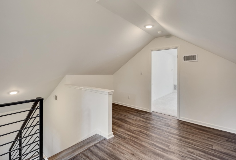 Loft space featuring wood-finish flooring, recessed lighting, and a contemporary black metal railing