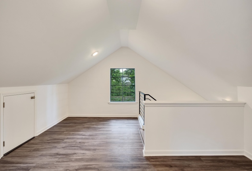 Spacious loft area featuring sloped ceilings with recessed lighting, dark wood-finish flooring, and a window with exterior views