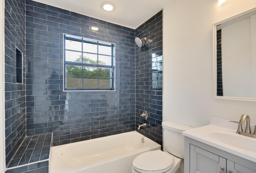 Bathroom featuring a subway-tiled tub/shower combination with an integrated niche and bench, a window with exterior grating, and a vanity with a white countertop