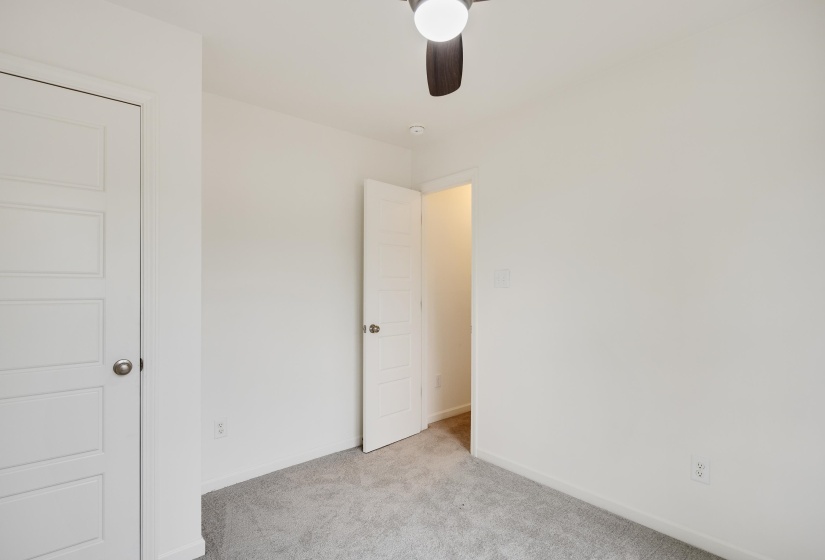 Crisp white walls define this room, featuring light gray carpeting and a contemporary ceiling fan with integrated lighting