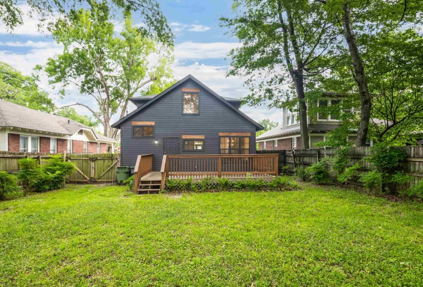 Rear exterior featuring dark siding, a wooden deck, and a spacious grassy yard