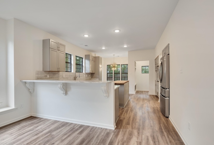 Kitchen featuring wood-finish flooring, light grey cabinetry, stone-look countertops with a matching backsplash, a central island with a wood-finish top, and stainless steel appliances