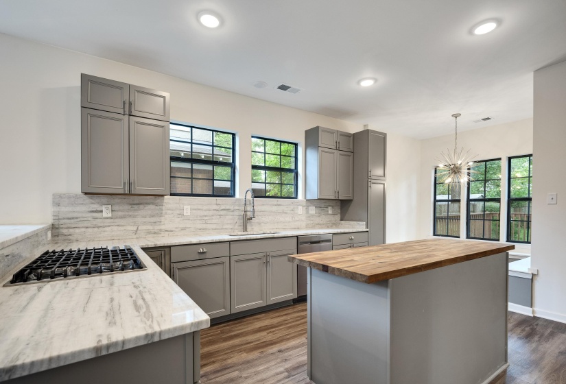 Modern kitchen featuring gray shaker cabinetry, integrated gas cooktop, light-toned countertops with matching backsplash, wood-finish flooring, and a central island with a butcher block top