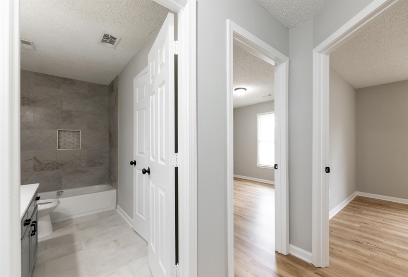 Hallway featuring a full bathroom with a tiled shower surround and a white bathtub, alongside two separate entrances to rooms with wood-finish flooring