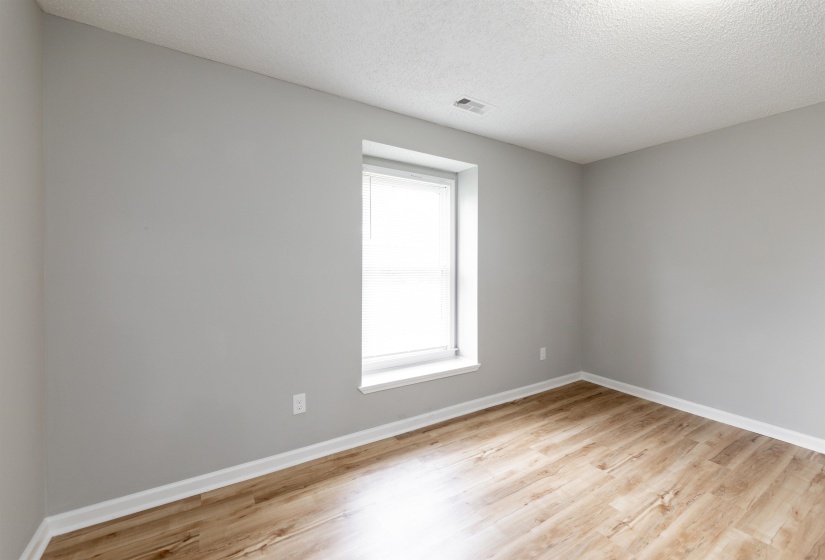 Bright room featuring a single window, light gray walls, wood-finish flooring, white baseboards, and a textured white ceiling