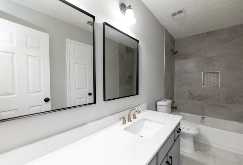 Bathroom featuring a vanity with an integrated sink, dual mirrors with black frames, a bronze-finish faucet, and a shower-tub combination with large format wall tiles and a recessed niche