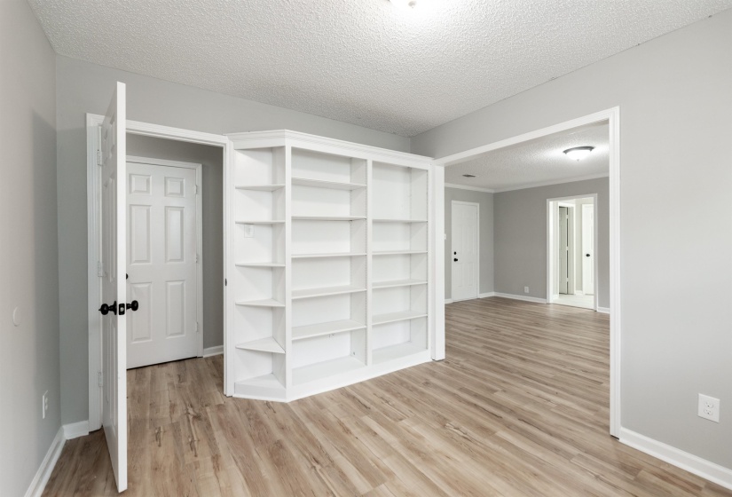 Integrated corner shelving unit, wood-finish flooring, light gray wall paint, white trim, and a semi-flush ceiling light fixture