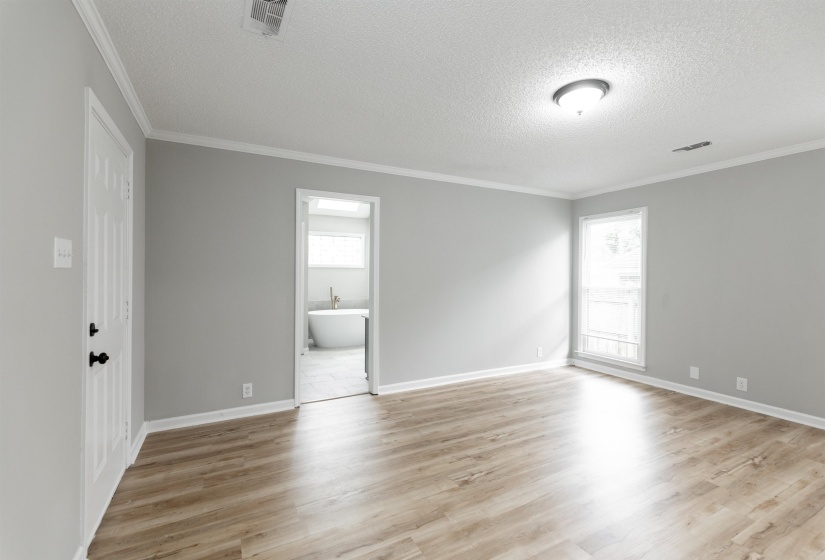 Spacious room featuring wood-finish flooring, light grey walls, and white crown molding