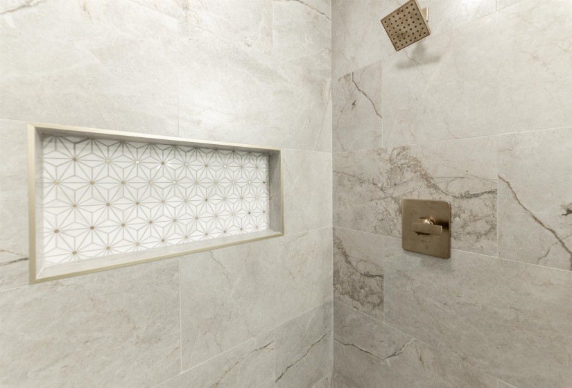 Shower with large format veined wall tiles, a built-in niche featuring geometric mosaic tile, and a square rain showerhead with coordinating controls