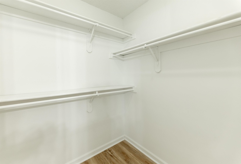 Walk-in closet featuring white walls, wood-finish flooring, white baseboards, and built-in white wire shelving and hanging rods