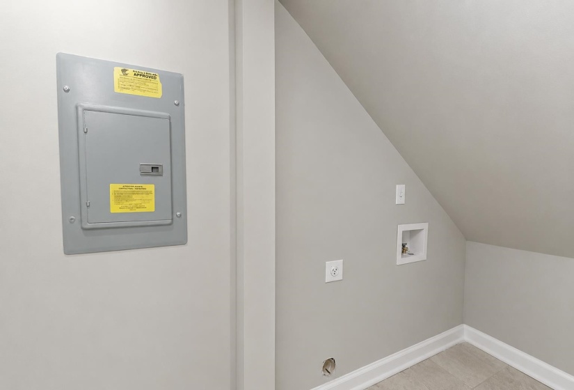 Utility area featuring a circuit breaker panel, wall outlet, and plumbing hookups