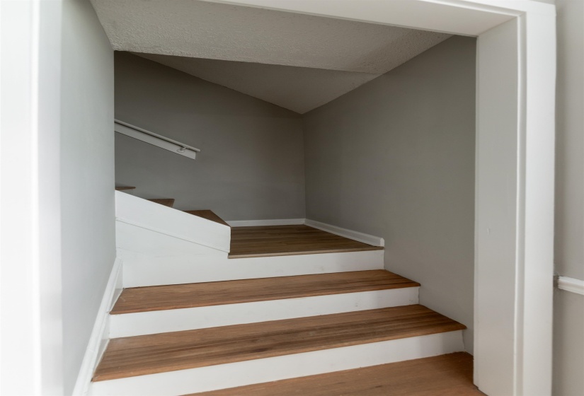 Staircase featuring wood-finish treads, white risers, and a white handrail set against light gray walls