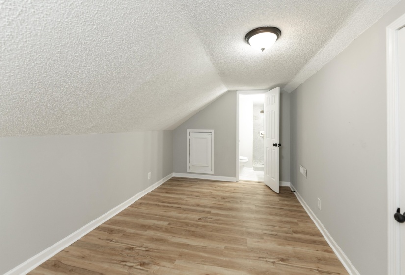 Attic room with wood-finish flooring, light gray walls, and a sloped ceiling