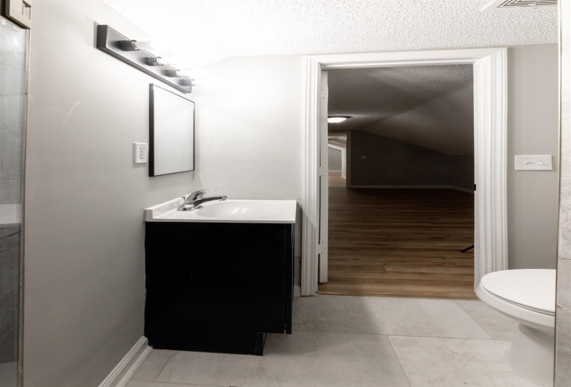 Bathroom featuring a modern black vanity with a white countertop and integrated sink, a rectangular mirror, and a contemporary four-bulb vanity light fixture
