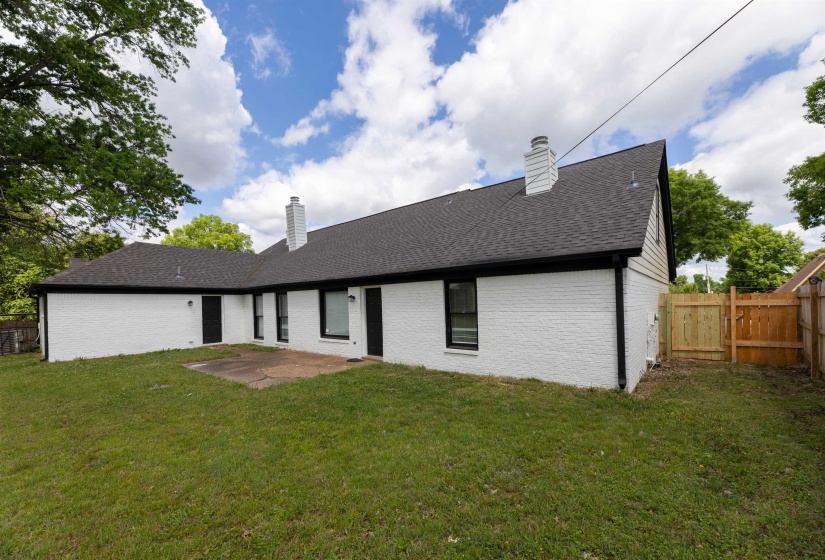 Expansive backyard featuring a manicured lawn, white brick exterior, black trim windows, a concrete patio, and a wood privacy fence