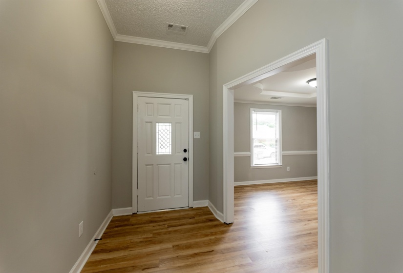 Entryway featuring wood-finish flooring, a paneled door with decorative glass insert, and crown molding