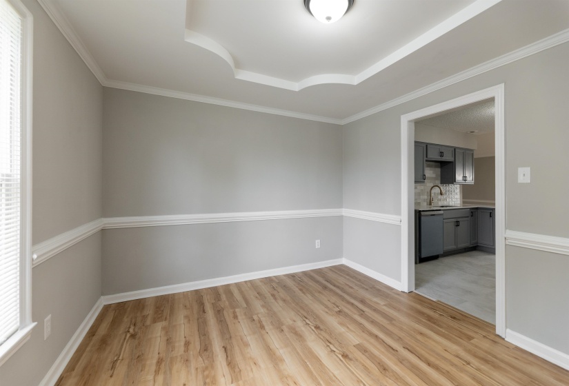 Spacious interior room featuring wood-finish flooring, chair rail molding, and a decorative tray ceiling