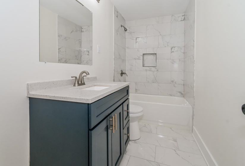 Bathroom featuring a dark blue vanity with gold-tone hardware, a light-toned countertop with an integrated sink, and a brushed nickel faucet