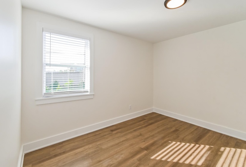 Room featuring wood-finish flooring, crisp white baseboards, a window with venetian blinds, and a flush-mount ceiling fixture