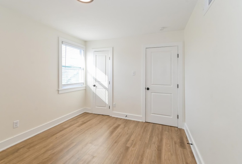 Room with wood-finish flooring, white baseboards, and two paneled interior doors with matte black hardware