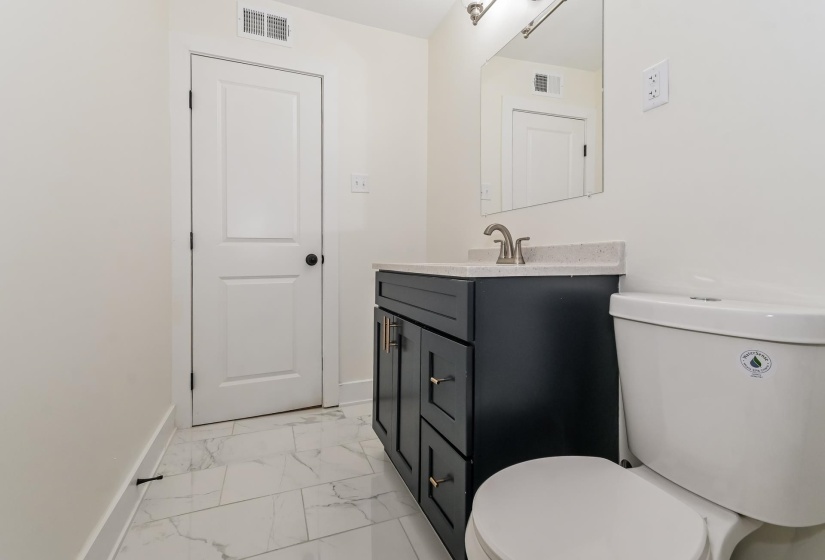 Bathroom featuring a dark wood-finish vanity with brass hardware, a light-toned countertop, a rectangular mirror, and white tile flooring