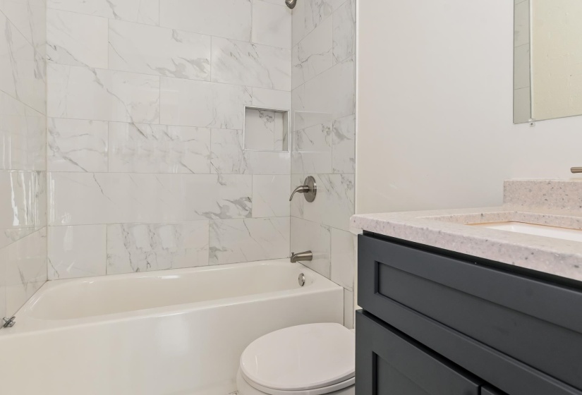 Bathroom featuring a white bathtub with a tiled surround, a built-in shower niche, and brushed nickel fixtures