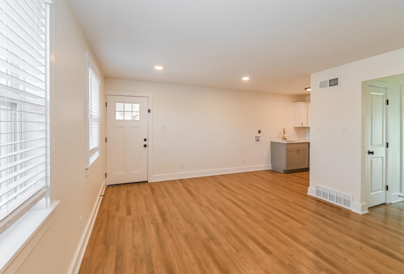 Open-concept living area with wood-finish flooring, recessed lighting, and a paneled entry door with clear glass inserts
