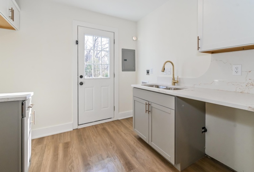 Utility area featuring a glass-paneled exterior door, wood-finish flooring, white walls, gray lower cabinetry, and light-toned countertops with a gold-finish faucet