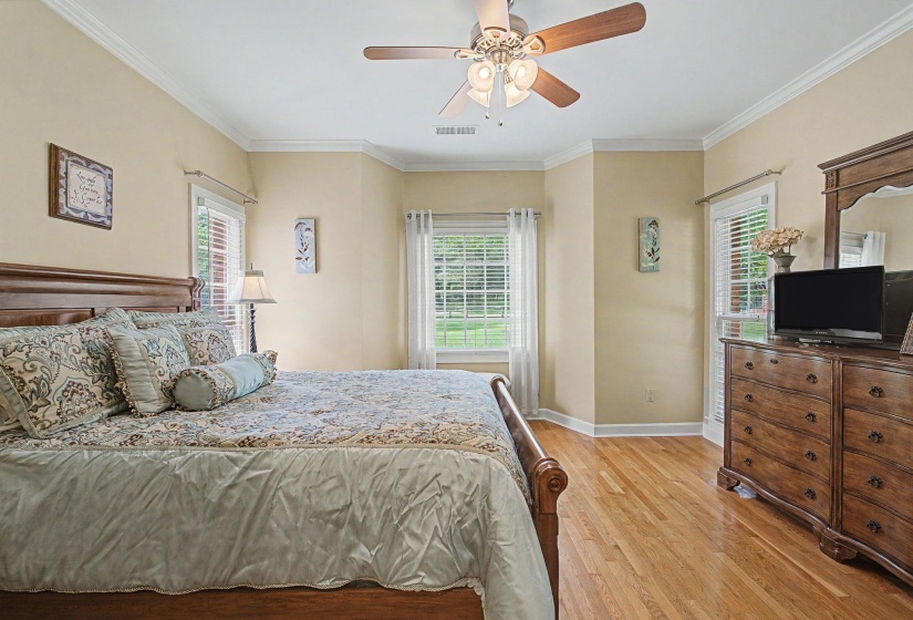 Spacious room featuring hardwood flooring, crown molding, a ceiling fan, and multiple windows with plantation-style blinds