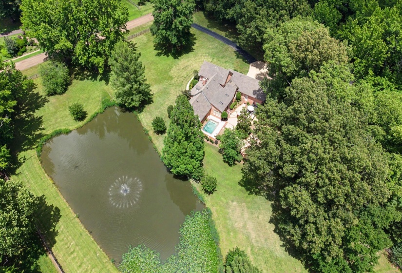Expansive property featuring a private pond with fountain, mature trees, a multi-wing residence with a tile roof, and an in-ground swimming pool