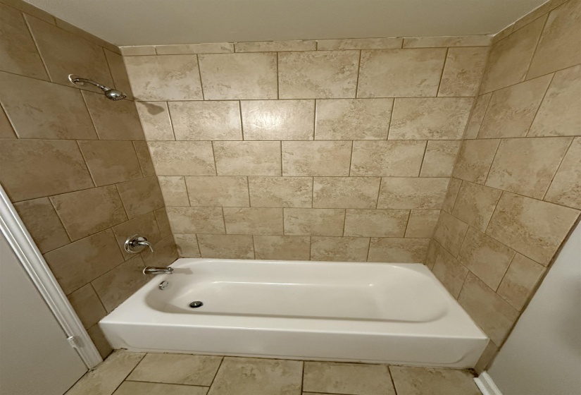 Shower and tub combination featuring ceramic tile surround, chrome fixtures, and a white porcelain tub