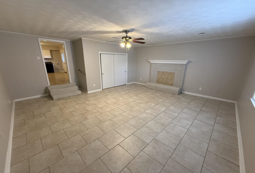 Spacious room featuring neutral tile flooring, a built-in fireplace with a tile surround and mantel, and white bi-fold closet doors