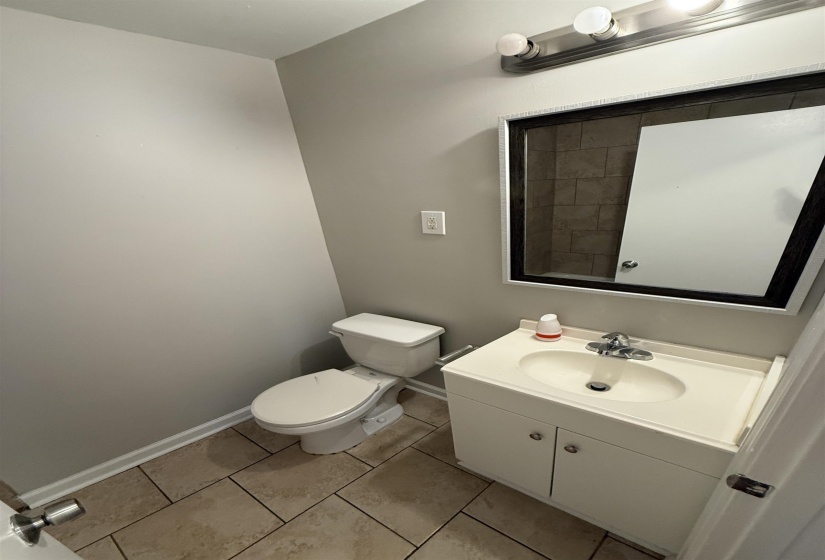Bathroom featuring a vanity with an integrated sink and base cabinetry, a wall-mounted mirror, overhead vanity lighting, a commode, and tile flooring