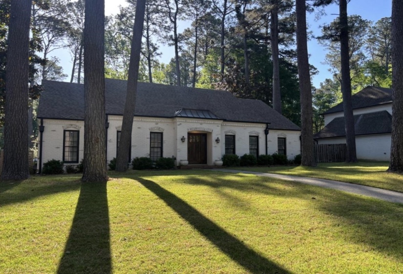 Exterior featuring a white brick facade, dark shingle roof, and a prominent wood entry door