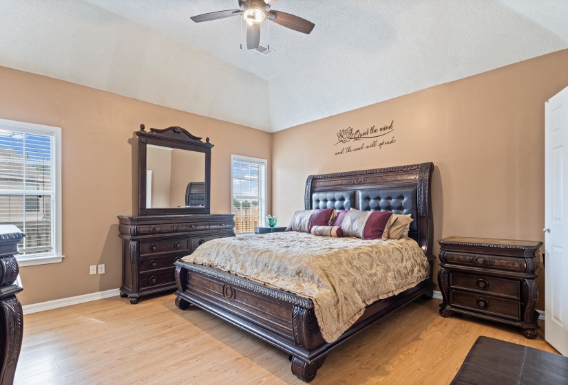 Vaulted ceiling bedroom featuring wood-finish flooring, a ceiling fan with integrated lighting, and two windows with blinds