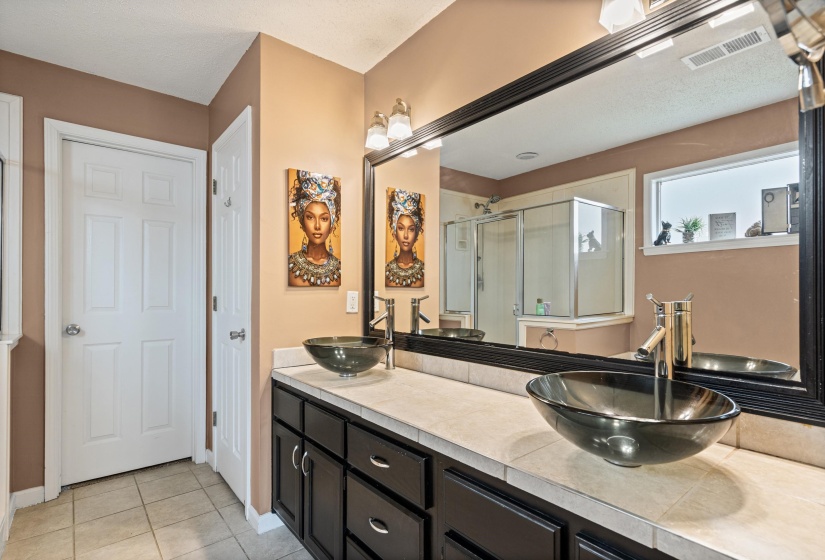 Double vanity with vessel sinks, dark wood-finish cabinetry, a large framed mirror, and tiled flooring