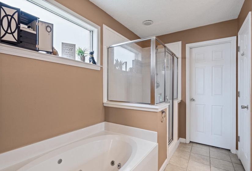 Built-in jetted tub featuring white surround, an adjacent glass-enclosed shower, transom window, and paneled interior door