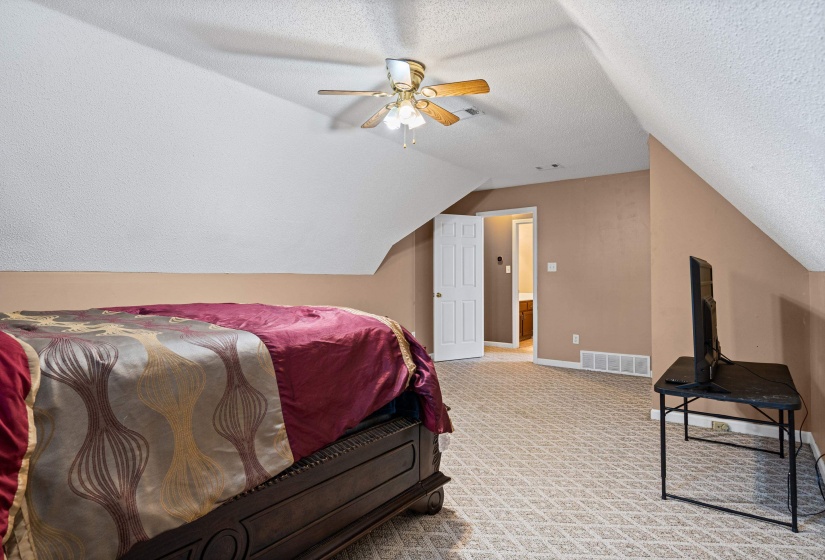 Sloped ceiling room featuring textured beige carpeting and a ceiling fan