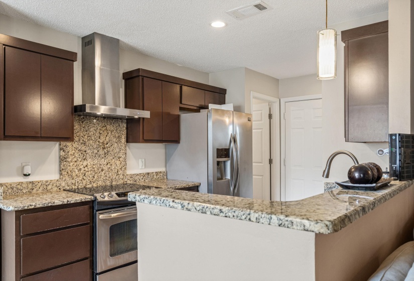 Kitchen featuring dark wood cabinetry, stainless steel appliances, speckled stone countertops, and a coordinating stone backsplash