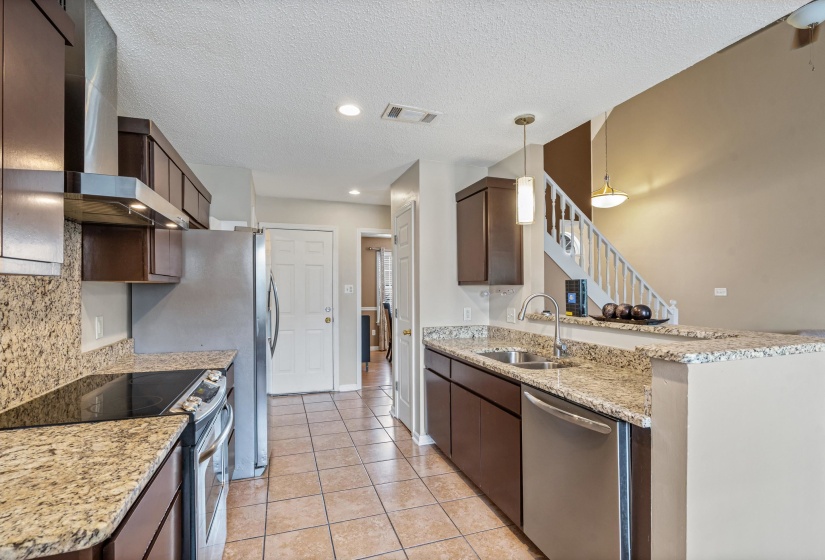 Kitchen featuring granite countertops, dark wood-finish cabinetry, stainless steel appliances, and tile flooring