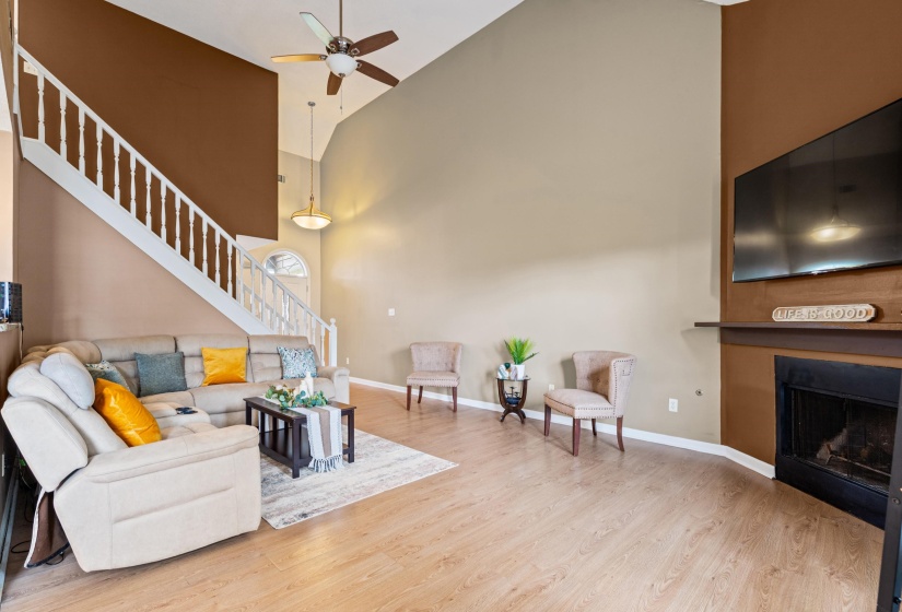 Vaulted living area featuring wood-finish flooring, a fireplace with a mantel, and a ceiling fan