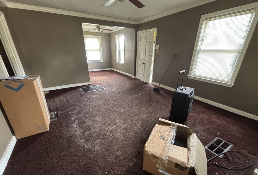 Spacious interior room with crown molding, ceiling fan, and multiple windows with blinds