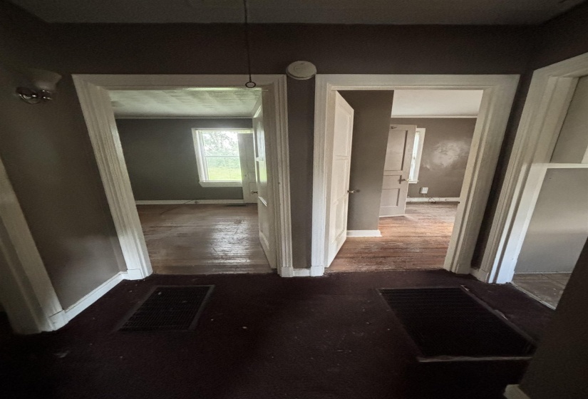 Interior hallway with two doorways featuring white trim, leading to separate rooms with wood-finish flooring