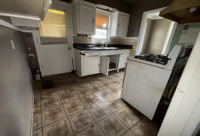Kitchen featuring patterned floor tiles, white cabinetry, a sink with dark countertops, and a window with blinds