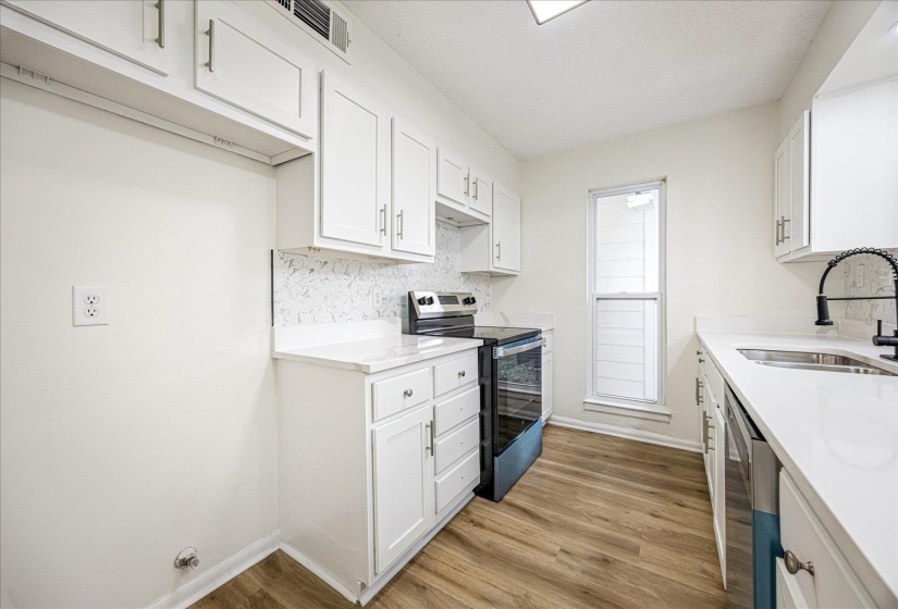 Kitchen featuring white cabinetry, stainless steel appliances, light wood finished floors, light stone countertops, and a textured ceiling