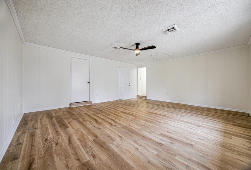 Spare room with attic access, light wood-style floors, ornamental molding, ceiling fan, and a textured ceiling