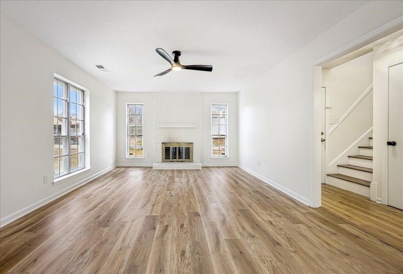 Unfurnished living room featuring stairs, a brick fireplace, light wood finished floors, a ceiling fan, and a textured ceiling
