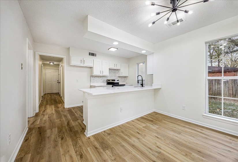 Kitchen with white cabinets, a peninsula, a chandelier, light wood-style flooring, and a textured ceiling